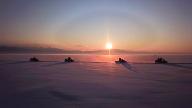 Unique flight close with snowmobiles fast speed ride Arctic extreme. Group of tourists no face in helmets. Clear sky sunny sunset horizon. Aerial drone footage.
