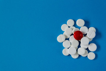 heap of white pills and one red, on a blue background