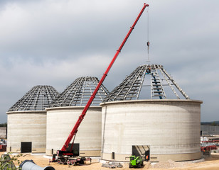  Crane on construction site. Large reinforced concrete tanks with metal roof construction