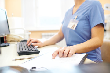 Close-up of unrecognizable nurse sitting at desk and using computer while analyzing medical notes