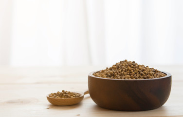 Coriander seeds in wooden bowl and spoon on wooden table background