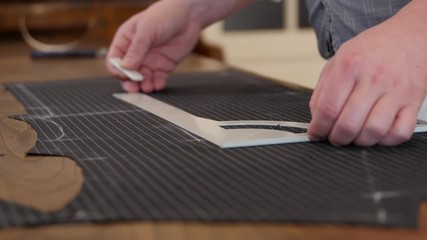 tailor drawing lines on a fabric with his chalk in order to make a bespoke suit-flat profile with anthracite wool made cloth. this stylist working in shop, drawing & cutting templates.