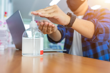 [Coronavirus] Freelance man working from home wearing protective mask. Freelance man in quarantine for coronavirus wearing protective mask. Working from home. Cleaning hands with sanitizer gel.