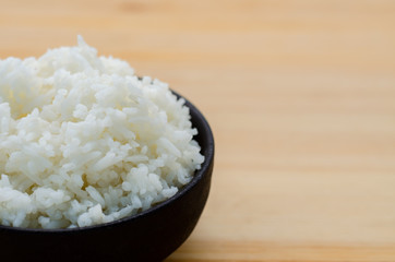Rice in the black bowl on wooden table background