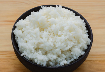 Rice in the black bowl on wooden table background