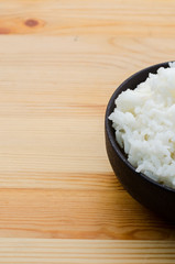 Rice in the black bowl on wooden table background