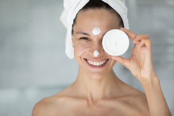 Close up woman with cream on face towel on head hold jar advertises anti-wrinkle remedy, deep...