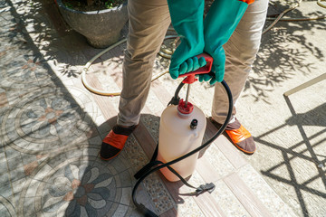 Coronavirus Pandemic. A disinfector in a casual dress and mask sprays disinfectants in front of house.