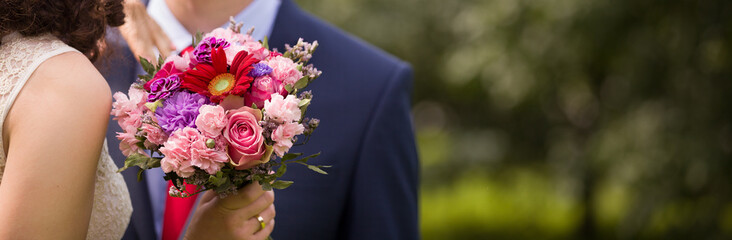 Happy couple hugging while standing in a park. A couple holding a beautiful wedding bouquet,...