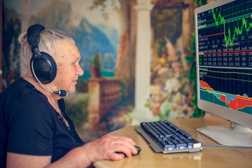 An elderly grandmother - a pensioner sits at a computer, studying brokerage, the stock market