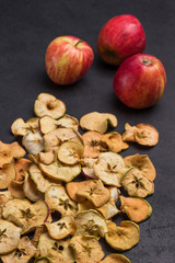 Fototapeta premium Three fresh red apples and slices of dried apples on black background.