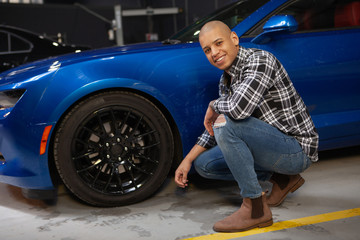 Cheerful attractive African man smiling to the camera while working at his garage with his new sports car