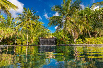 Tropical swimming pool, waterfall and jungle nature with palm trees under blue sky. Luxury summer...
