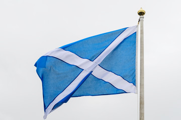 Flag of Scotland (Saltire or the Saint Andrew's Cross) blowing in the wind towards cloudy grey sky in a rainy day 
