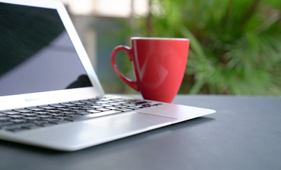 Computer laptop with offee in red cup with green nature background. Work remotely or from home.