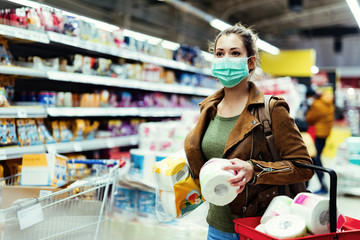 Fototapeta premium Woman with face mask making stock of toilet paper while buying in supermarket.