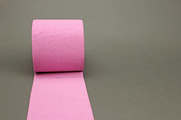 Roll of pink toilet paper on dark grey background. Space for text