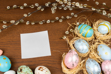 Empty white paper on a wooden table framed with easter eggs and willow twigs