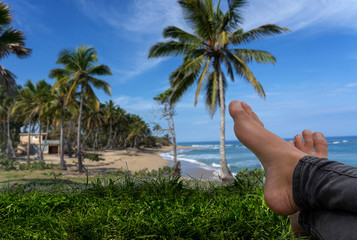 Feet girl relaxing in the foreground against a Caribbean beach background. Blue sky and palm trees.