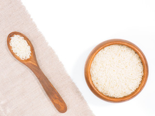Indian long grain Basmati rise in wooden spoon diagonally and wooden bowl on white and beige fabric background