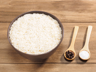 Long grain Basmati rice in brown ceramic bowl, allspice, salt on brown wooden background