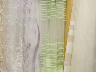 Light colored fabrics with a pattern hang for sale in a store. The concept of fashionable clothes and interior