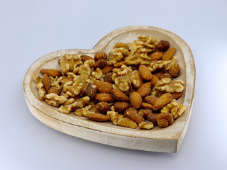 Mix of different nuts on the plate: almond, hazelnut, walnut in a heart form on the white background