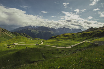 Panorama from Grossglockner pass at Hochtor on a summer day with beautiful clouds, green meadows and winding road seen below. Summer on mountain pass.