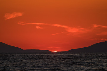 Evening view of croatian coast close to Karlobag with sunset around island of Pag and Rab. Sun just about to set behind two hills into the sea.