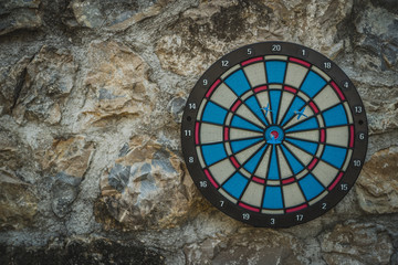 Round dartboard in black, red, blue and white hanging on a vintage stone wall outside. Garden or porch entertainment.