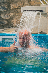 Young caucasian male with bald head enjoying a flow of water fountain flowing onto his head inside...
