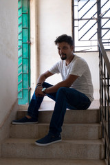 Portrait of a handsome brunette Indian bengali smart man in shirt and trousers sitting in the stair...