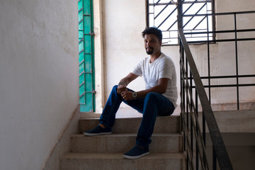 Portrait of a handsome brunette Indian bengali smart man in shirt and trousers sitting in the stair...