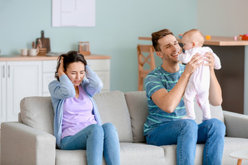 Happy father with his baby and wife suffering from postnatal depression at home