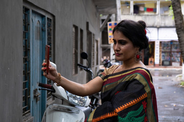 Portrait of a beautiful brunette Indian bengali thoughtful woman in traditional wear sari standing...
