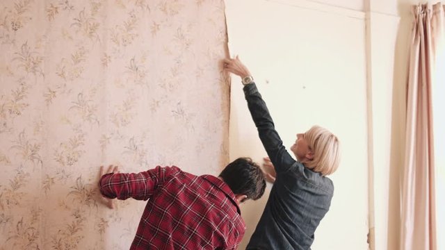 Adult couple home improvement taking of wallpaper