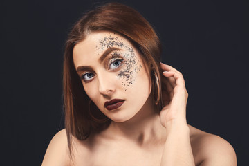 Fashionable young woman with glitters on her body against dark background