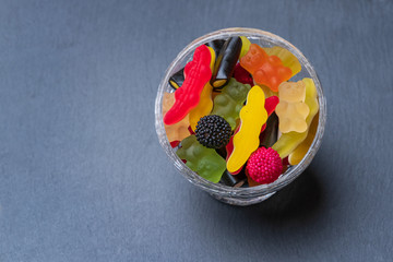 Colored candies inside a glass cup on dark background. Top view with space for your greetings