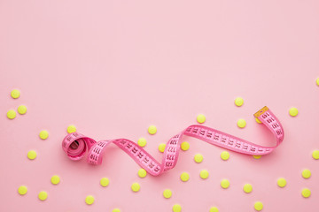 Measuring tape and weight loss pills on color background