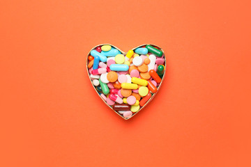 Heart made of pills on color background