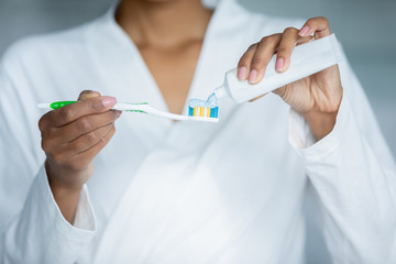 Mixed-race african woman do morning routine, female hands apply gel dentifrice toothpaste from tube...