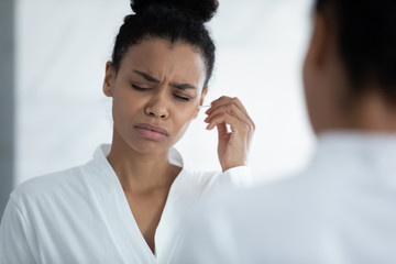 Unhealthy young African woman hold cotton bud cleaning ears removes earwax feels discomfort and...