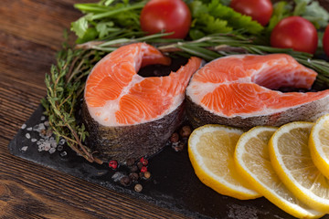 Two fresh salmon steakes with greenery, lemon and cherry tomatoes on the black board