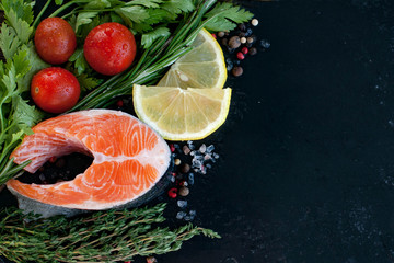 a fresh salmon steak with greenery, lemon and cherry tomatoes on the black board