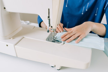 Woman hands using the sewing machine to sew the face home made diy medical mask during the coronavirus pandemia.