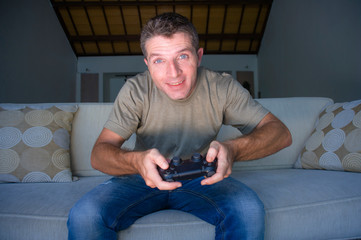 indoors portrait of young excited and happy man at home playing videogames holding controller...