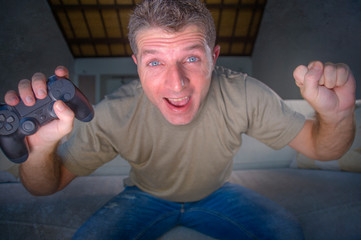 indoors portrait of young excited and happy man at home playing videogames holding controller...