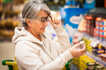 Senior woman at the supermarket reading the label carefully on a product. Active elderly people everyday life concept
