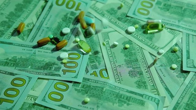 Medical expenses. Health insurance. Pills capsules scattering on 100 dollar bills.