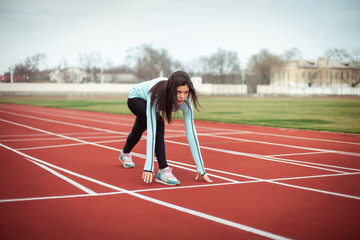  A beautiful girl performs sports exercises in a blue stadium with brown rubber tracks. Woman in a blue trowel and black leggings.